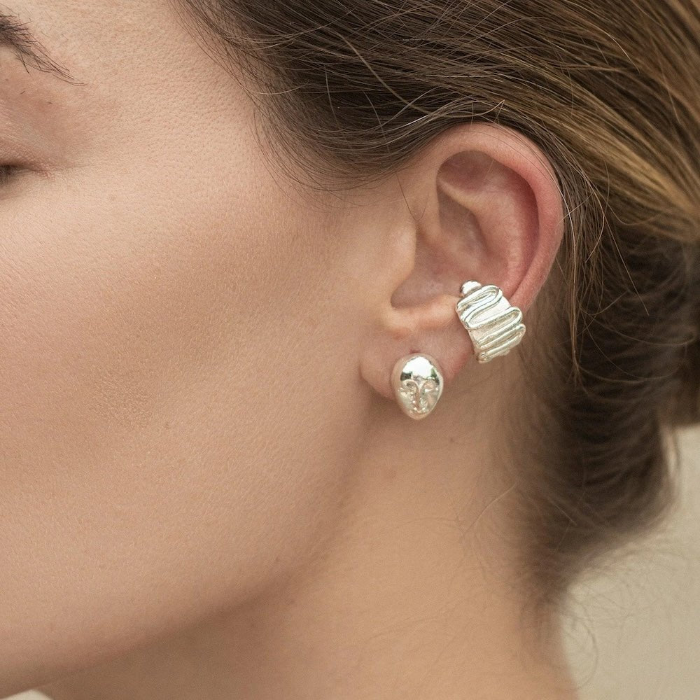 Close-up image of a woman wearing earrings in Silver. It's set against a white background. The purpose of this image is to highlight the earrings by Pajarolimon Jewelry.