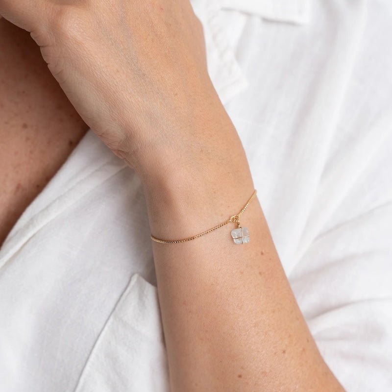 Close up image of a woman wearing a gold chain bracelet with an aquamarine stone on it. The purpose of the image is to highlight the bracelet because it is on sale at EVAMAIA boutique in Studio City, CA.