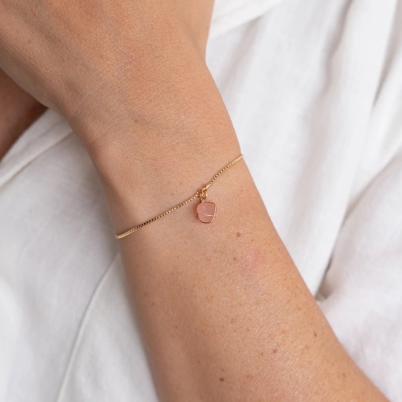 Close up image of a woman wearing a gold chain bracelet with an rose quartz stone on it. The purpose of the image is to highlight the bracelet because it is on sale at EVAMAIA boutique in Studio City, CA.