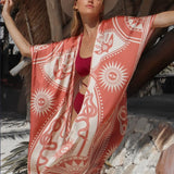 Image of a woman wearing a light saffron-colored kimono with the image of an eye, snakes, and the sun. The purpose of this image is to highlight the kimono, which is for sale at EVAMAIA boutique in studio city, CA.