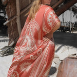 Image of a woman wearing a light saffron-colored kimono with the image of an eye, snakes, and the sun. The purpose of this image is to highlight the kimono, which is for sale at EVAMAIA boutique in studio city, CA.