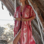 Image of a woman wearing a light red kimono with the image of an eye, snakes, and the sun. The purpose of this image is to highlight the kimono, which is for sale at EVAMAIA boutique in studio city, CA.