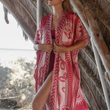 Image of a woman wearing a light red kimono with the image of an eye, snakes, and the sun. The purpose of this image is to highlight the kimono, which is for sale at EVAMAIA boutique in studio city, CA.