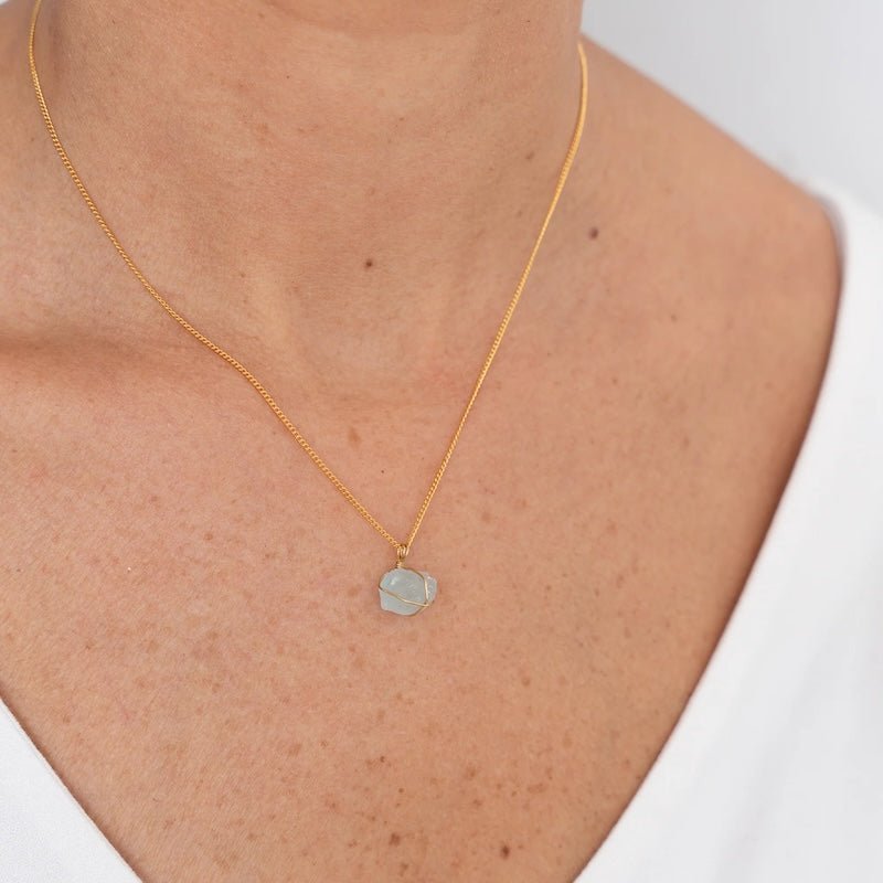 Close up image of a woman wearing a gold necklace with an aquamarine charm. The purpose of this image is to highlight the necklace by Wish Jewelry because it's sold at EVAMAIA boutique in Studio City, CA.