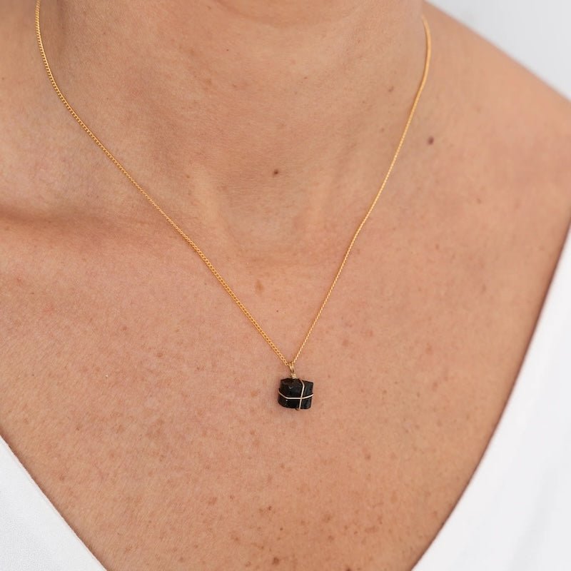 Close up image of a woman wearing a gold necklace with a black tourmaline charm. The purpose of this image is to highlight the necklace by Wish Jewelry because it's sold at EVAMAIA boutique in Studio City, CA.