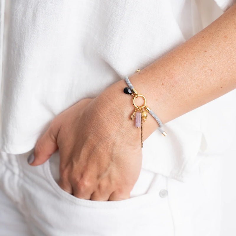 Close-up image of a woman wearing a thread bracelet with many charms. The purpose of this image is to promote the bracelet because it is for sale at EVAMAIA boutique in studio city, ca and online.