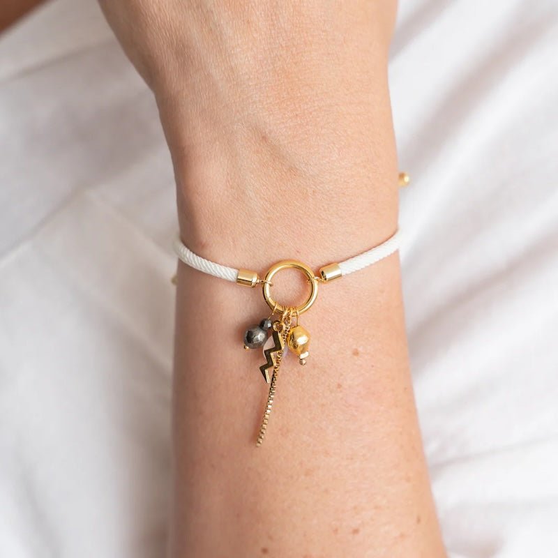 Close-up image of a woman wearing a thread bracelet with many charms, including a thunderbolt. The purpose of this image is to promote the bracelet because it is for sale at EVAMAIA boutique in studio city, ca and online.