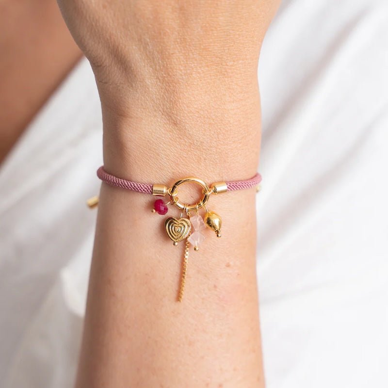 Close-up image of a woman wearing a thread bracelet with many charms. The purpose of this image is to promote the bracelet because it is for sale at EVAMAIA boutique in studio city, ca and online.