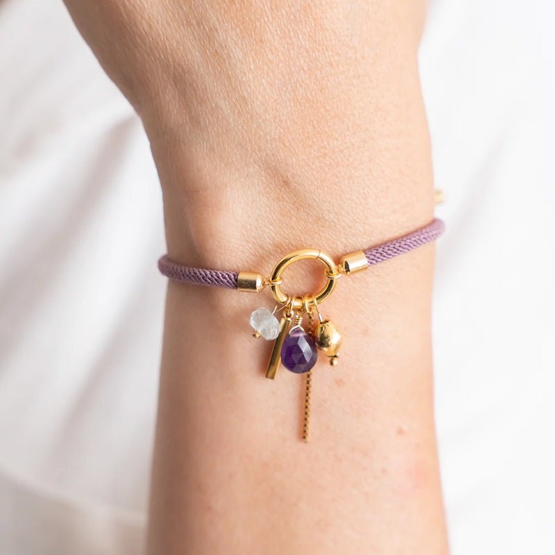 Close-up image of a woman wearing a thread bracelet with many charms. The purpose of this image is to promote the bracelet because it is for sale at EVAMAIA boutique in studio city, ca and online.