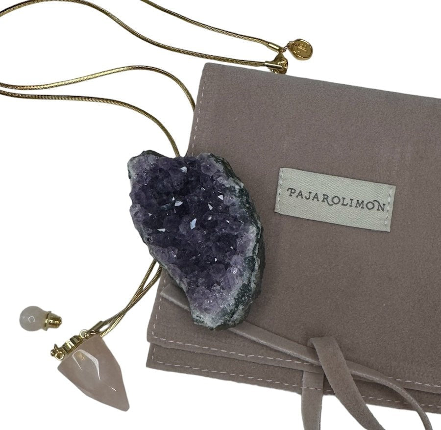 Image of a gold necklace holding a rose quartz perfume bottle. The purpose of this image is to highlight the necklace. This necklace is made in Colombia by Pajarolimon and sold at EVAMAIA boutique.