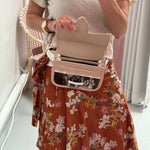 Woman wearing a carriel belt bag (and opening it) as she's taking a picture. She's wearing a flower skirt and white t-shirt.