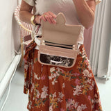 Woman wearing a carriel belt bag (and opening it) as she's taking a picture. She's wearing a flower skirt and white t-shirt.