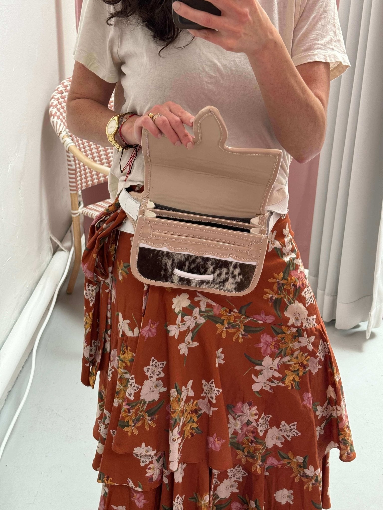 Woman wearing a carriel belt bag (and opening it) as she's taking a picture. She's wearing a flower skirt and white t-shirt.