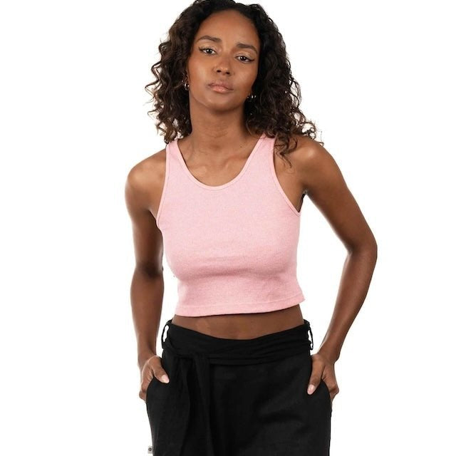 Woman wearing a pink ribbed top and black bottoms. She's standing by a white background and looking at the camera. The purpose of this image is to highlight the sustainable clothing by Madre Tierra.