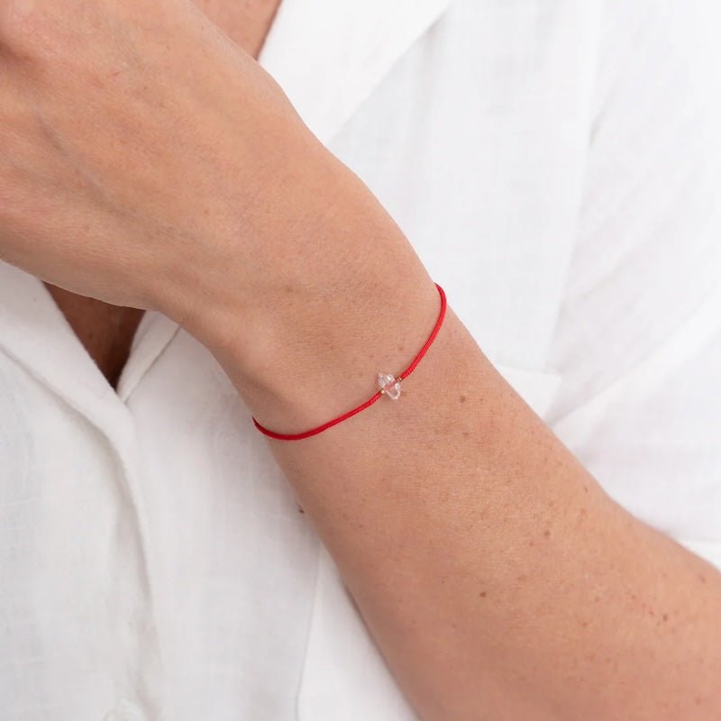 Close up image of a woman wearing a red threaded bracelet with a clear stone on it. A Herkimer diamond. The purpose of this image is to highlight the bracelet because it is for sale at EVAMAIA in Studio City, CA and online.