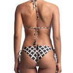 Close up of the back of a woman wearing a black and white bikini set. She's in front of a white background. The purpose of this image is to highlight the bikini, which is available for sale at EVAMAIA Boutique in Studio City, CA.