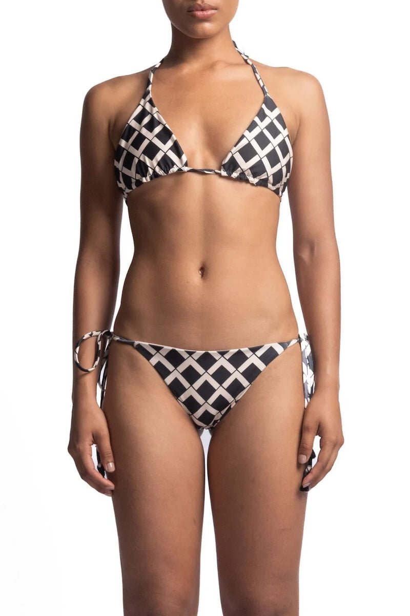 Close up of a woman wearing a black and white bikini set. She's in front of a white background. The purpose of this image is to highlight the bikini, which is available for sale at EVAMAIA Boutique in Studio City, CA.