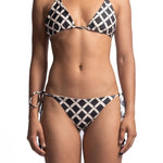 Close up of a woman wearing a black and white bikini set. She's in front of a white background. The purpose of this image is to highlight the bikini, which is available for sale at EVAMAIA Boutique in Studio City, CA.