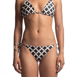 Close up of a woman wearing a black and white bikini set. She's in front of a white background. The purpose of this image is to highlight the bikini, which is available for sale at EVAMAIA Boutique in Studio City, CA.