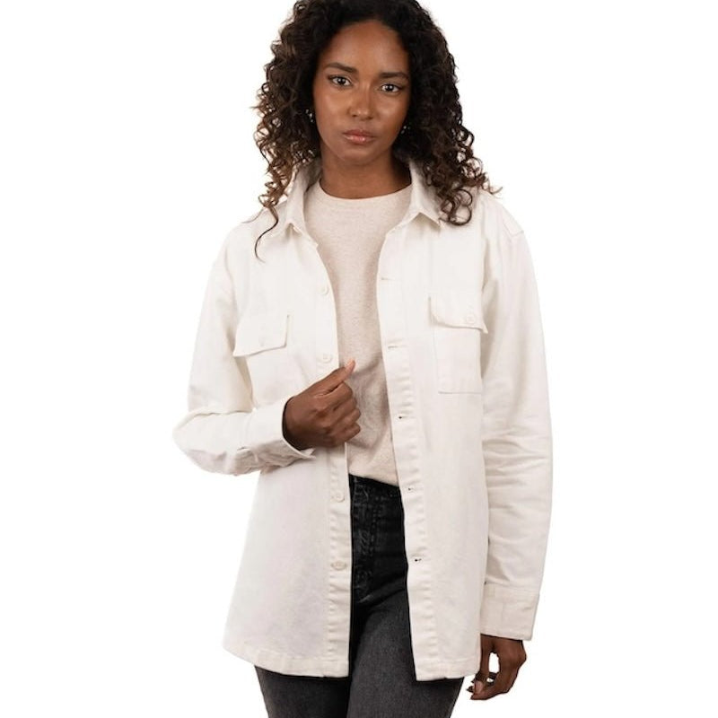 Woman wearing jeans, a t-shirt and a white jacket. She's standing behind a white background. The purpose of this image is to highlight the jacket, which is made in Colombia and available at EVAMAIA boutique.