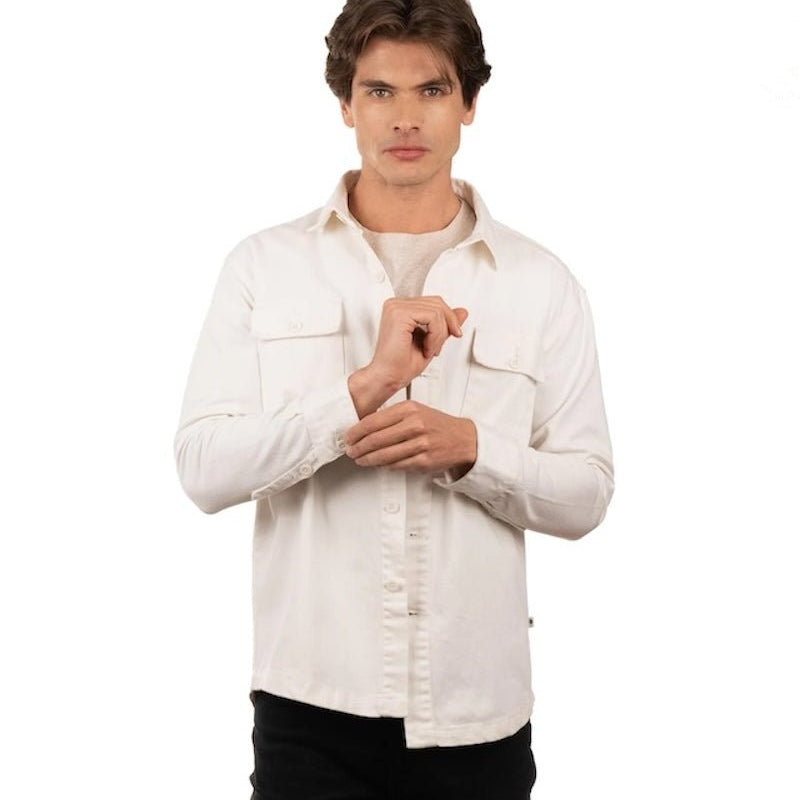 Man wearing jeans, a t-shirt and a white cotton jacket. He's standing behind a white background. The purpose of this image is to highlight the jacket, which is made in Colombia and available at EVAMAIA boutique.